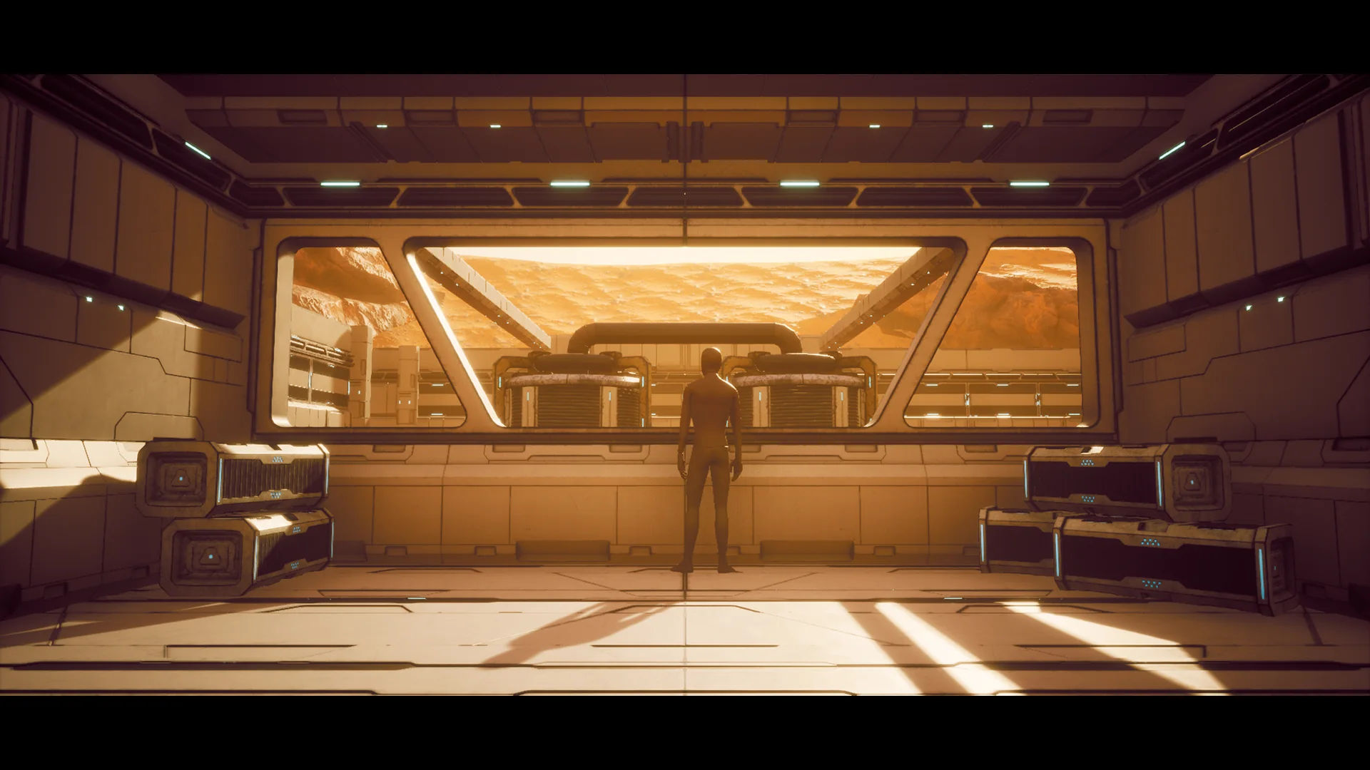 Wide interior bay looking out through a panoramic window onto the desert, with transport cases stacked along both walls and a figure for scale.